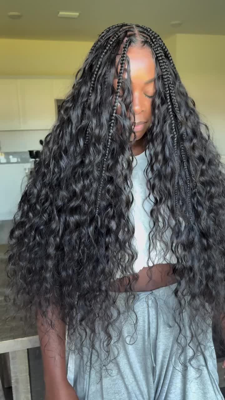 Long black knotless braids blend into loose curls over a gray top