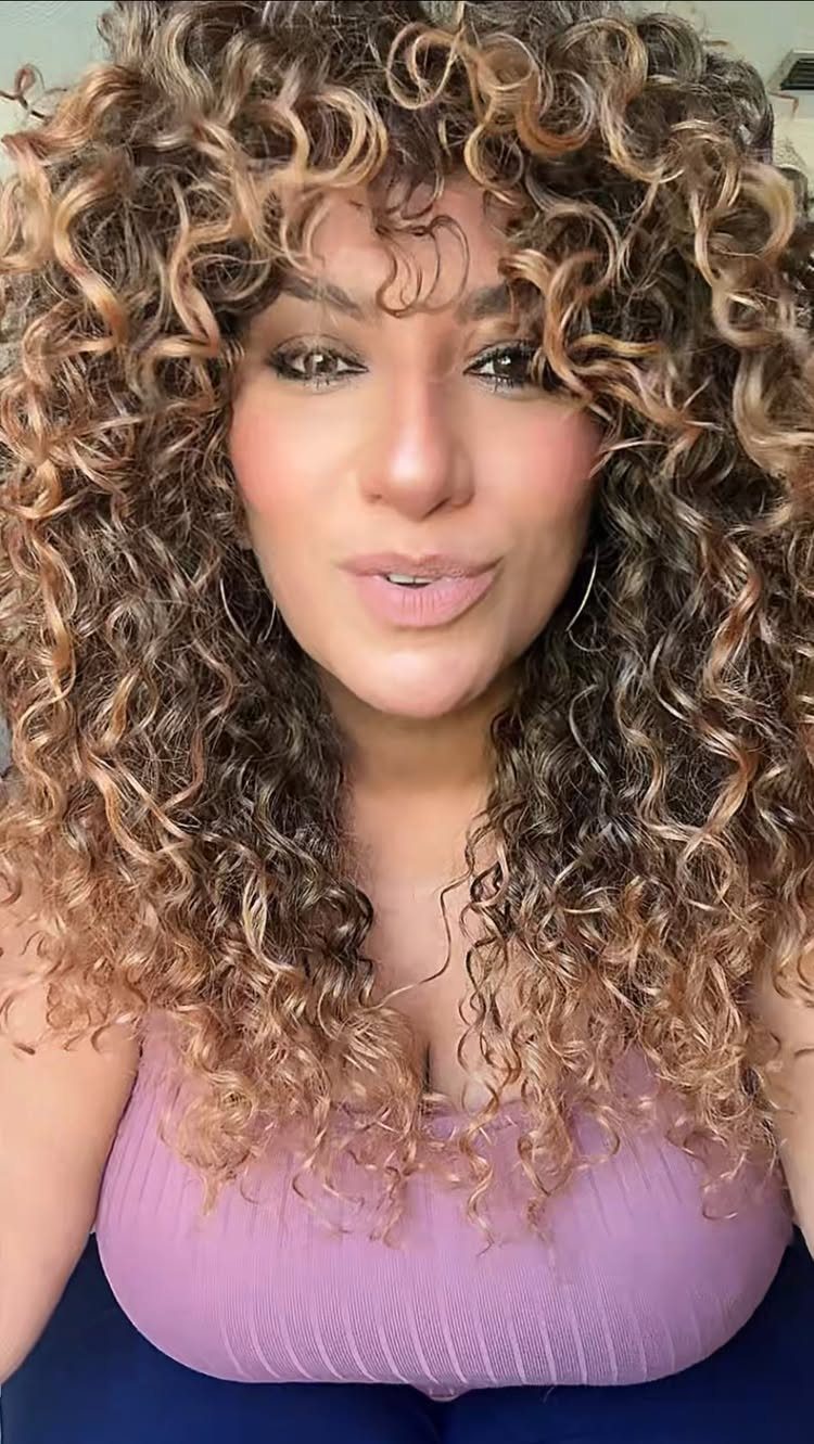 Woman showcasing long brown curls with a defined curly fringe and lavender sleeveless top