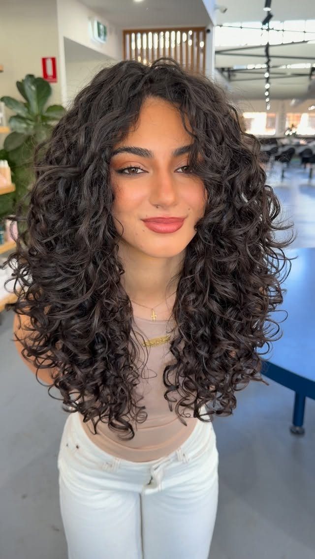 Woman showing long, layered dark curls in a bright hair salon