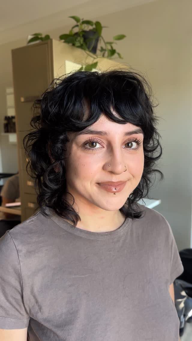 Dark curly mullet with short bangs and longer curls framing the face