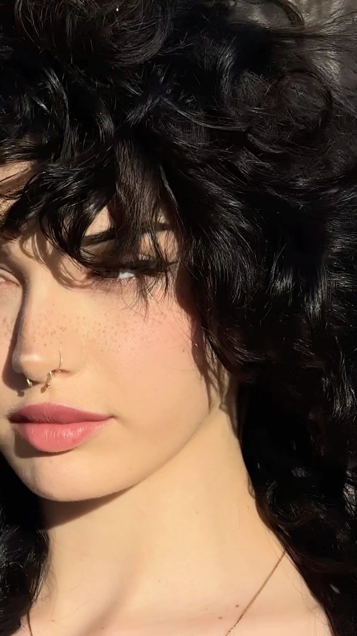 Person with voluminous dark curly shag layers and wispy bangs