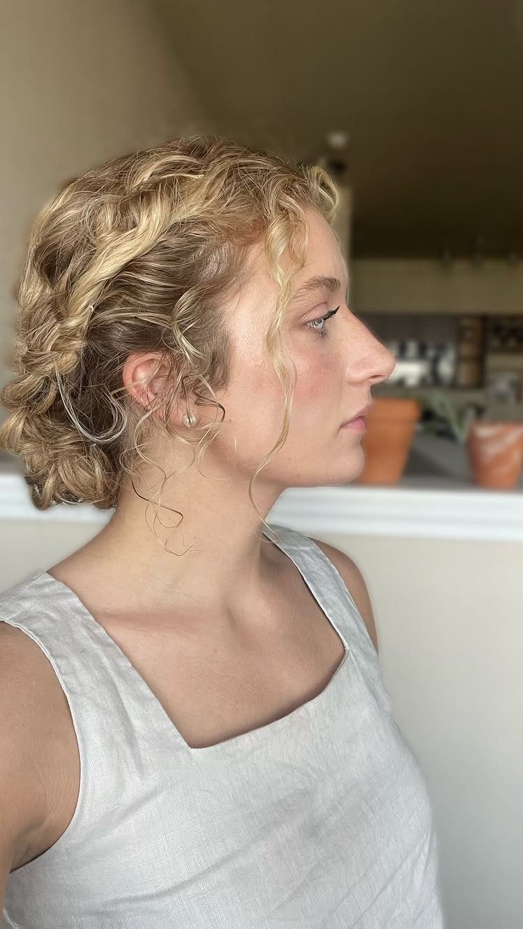 Blonde curly updo gathered at the back with loose tendrils around her face