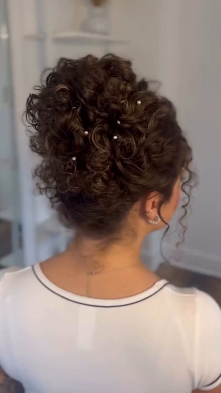 High curly bun piled loosely above a white shirt with dark trim