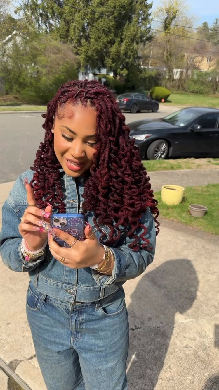 Woman with long burgundy dreadlocks and curled ends holding a phone