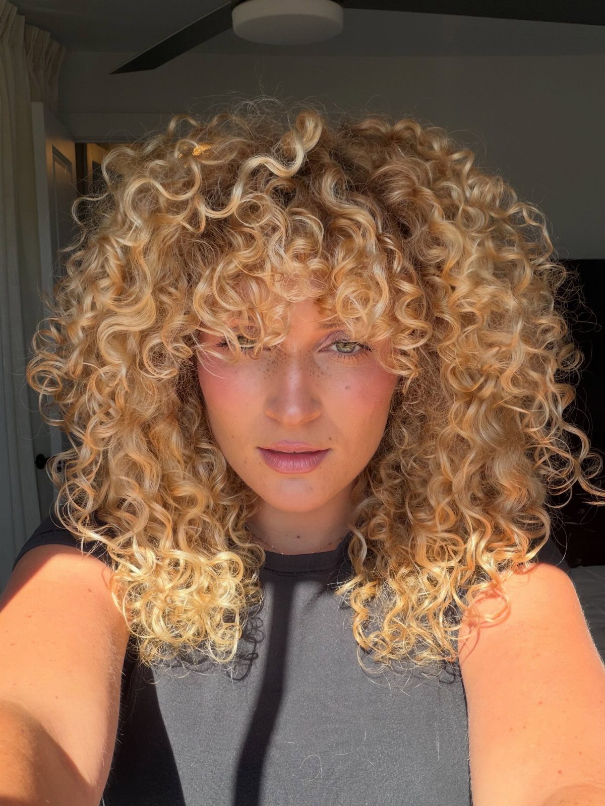 Tousled blonde curls with light tips frame a person’s face