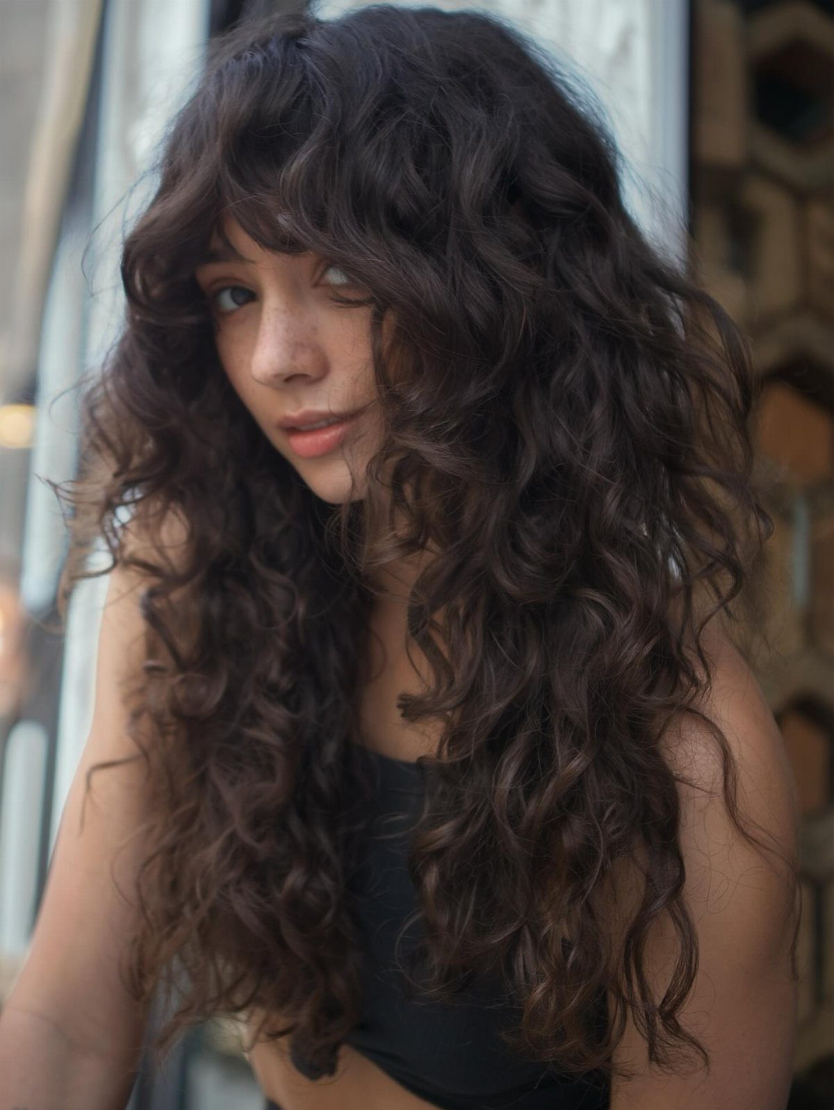 Woman with long dark curls and a choppy, uneven curly fringe