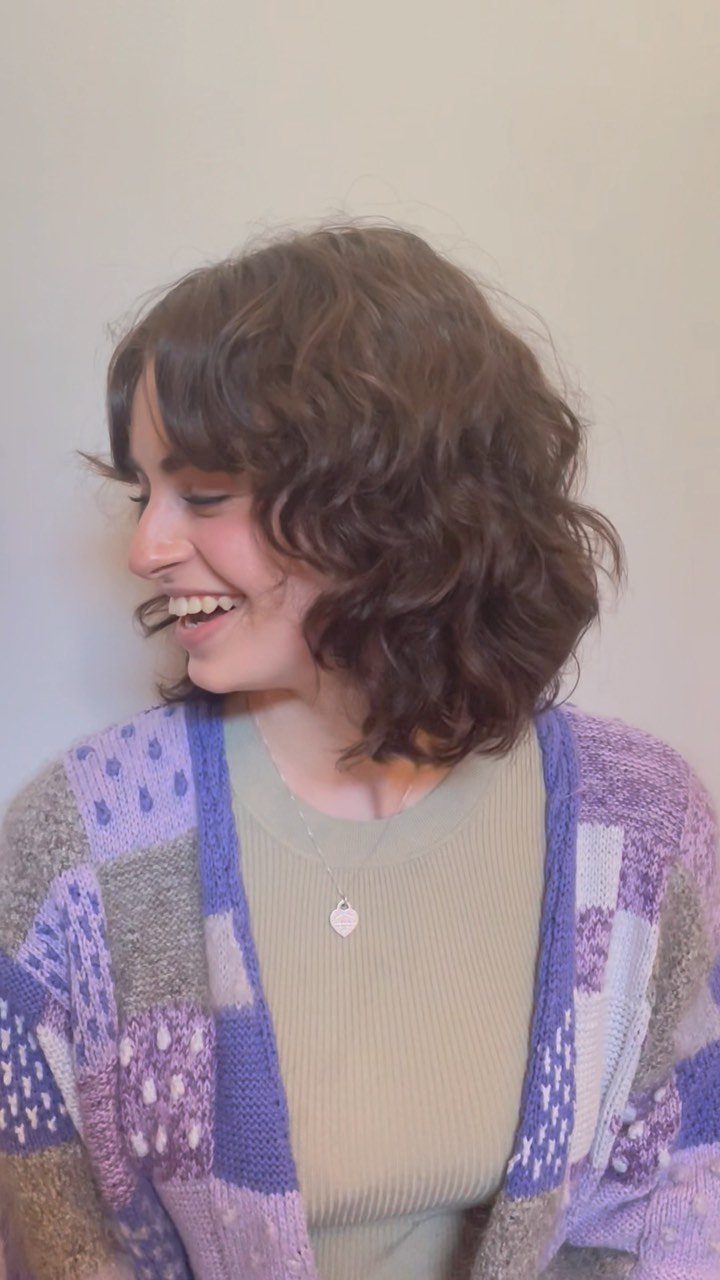 Curly-haired person with a face-framing fringe and shoulder-length layers