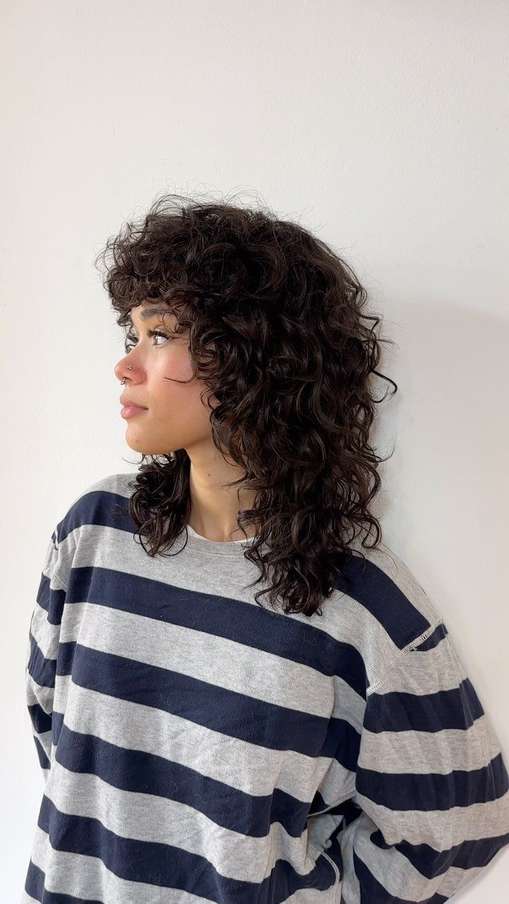 Person with voluminous dark curly shag and center-parted curtain bangs