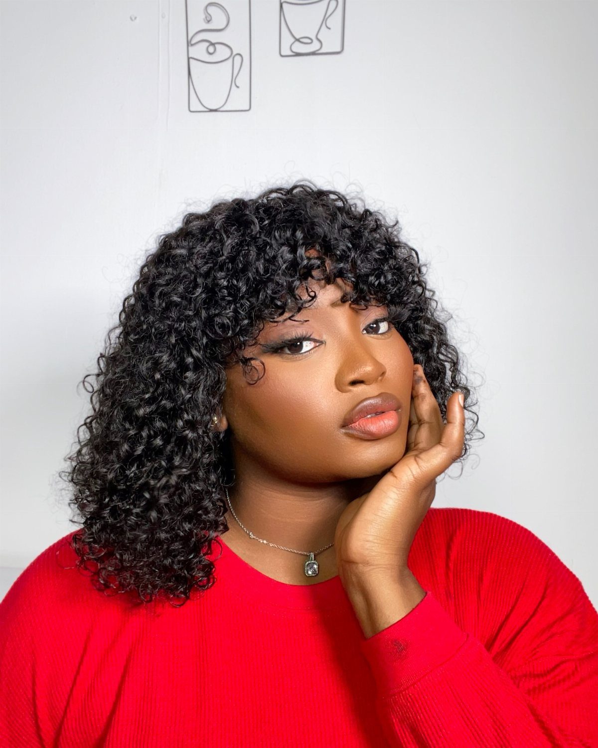 Woman with black ringlet curls and a soft curly fringe wearing a red top