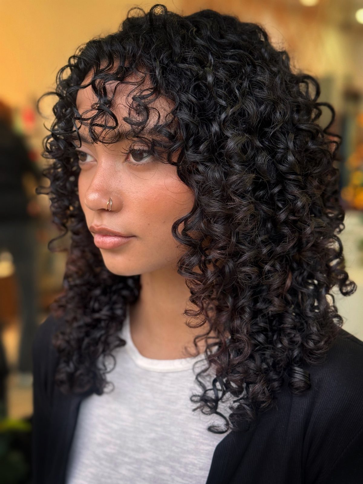 Person with long black curls and short curly bangs in side profile