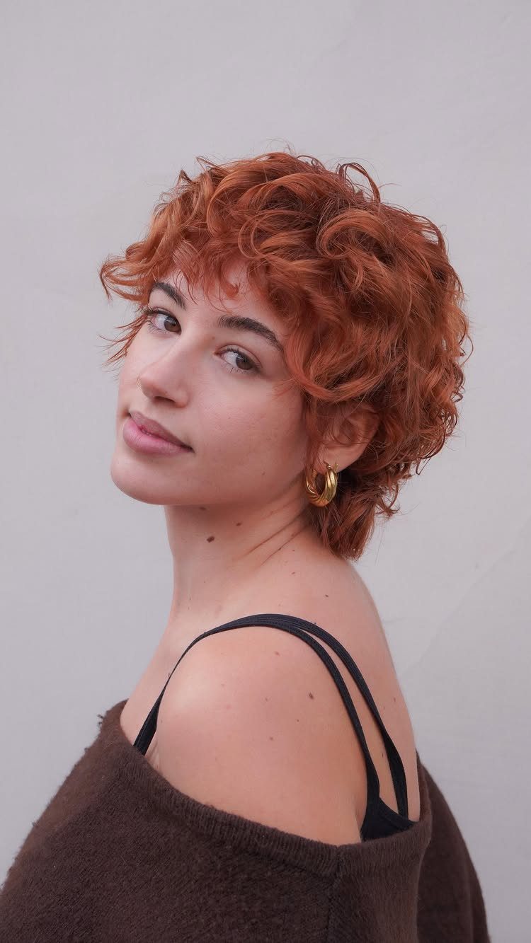 Person wearing a layered copper-red curly pixie with voluminous movable curls