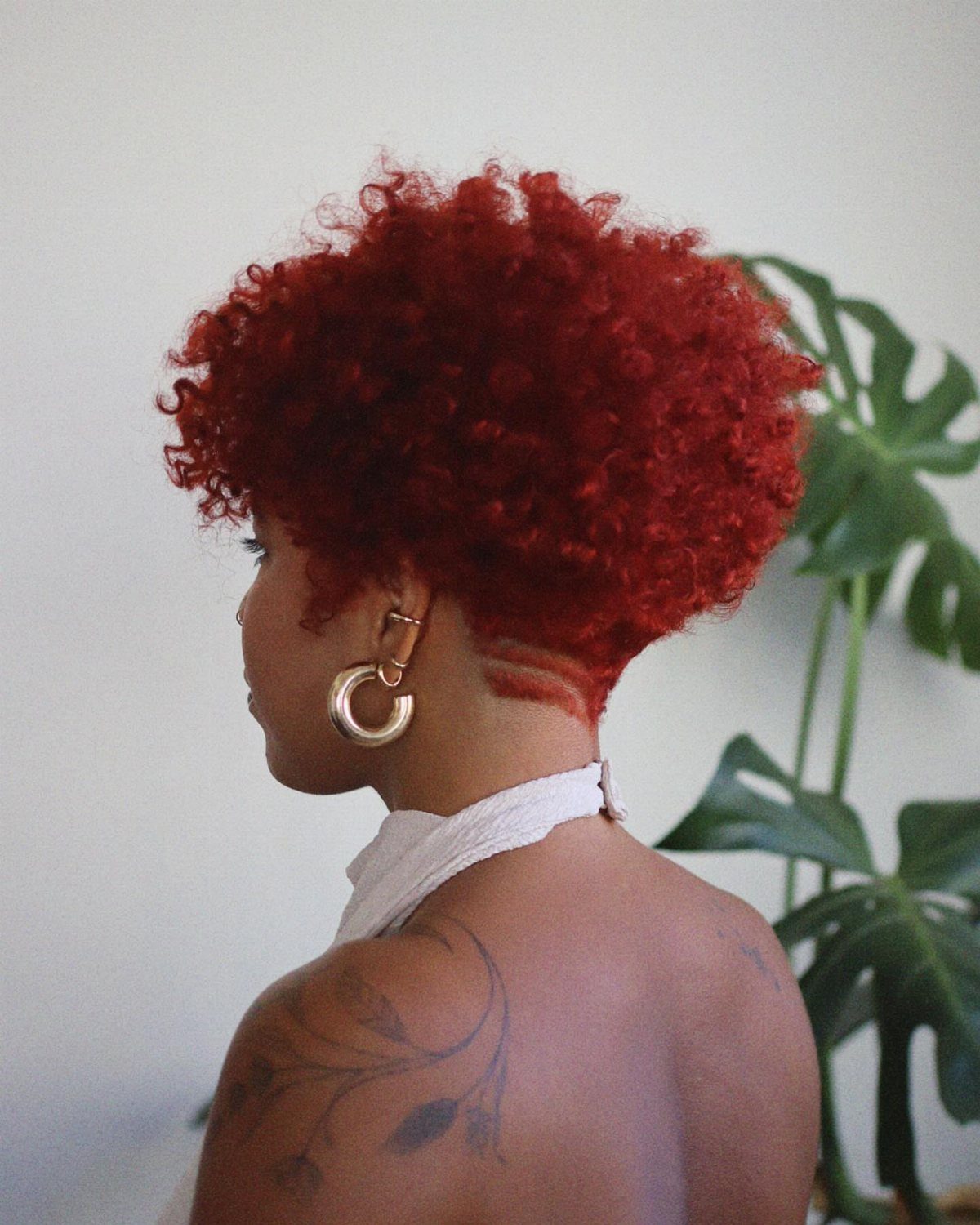 Short red curls form a voluminous pixie cut above a shaved nape