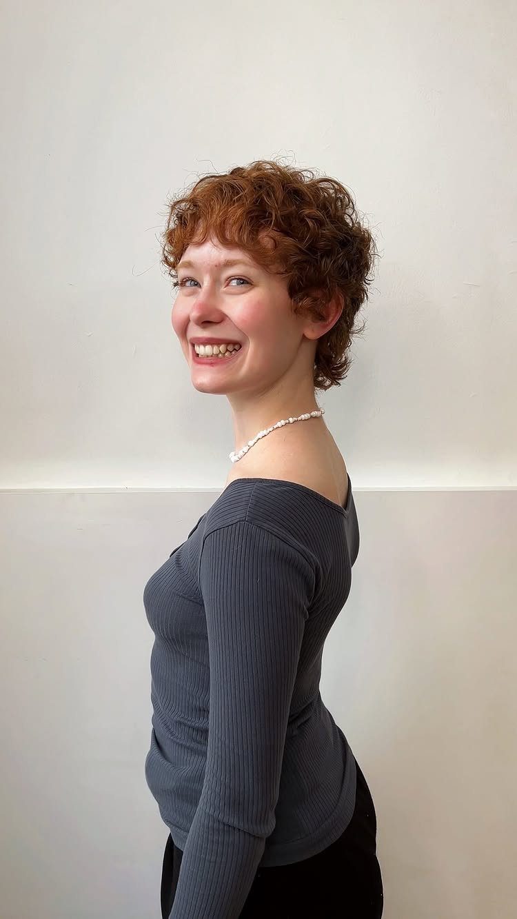Woman with short auburn curls framing her face, smiling in profile