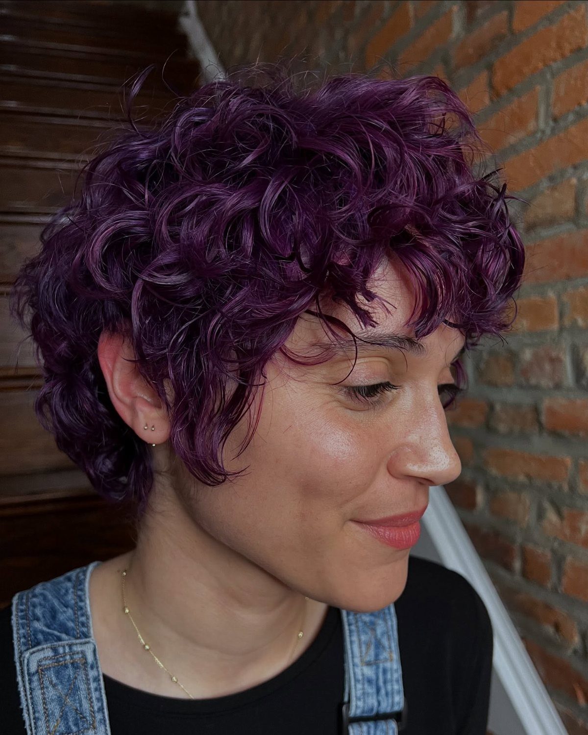 Person showcasing a short curly pixie haircut with rich purple-toned curls