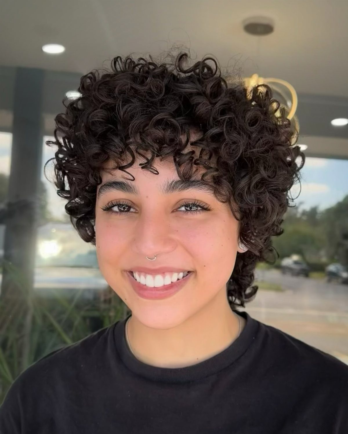 Smiling person showcasing a short curly dark pixie haircut