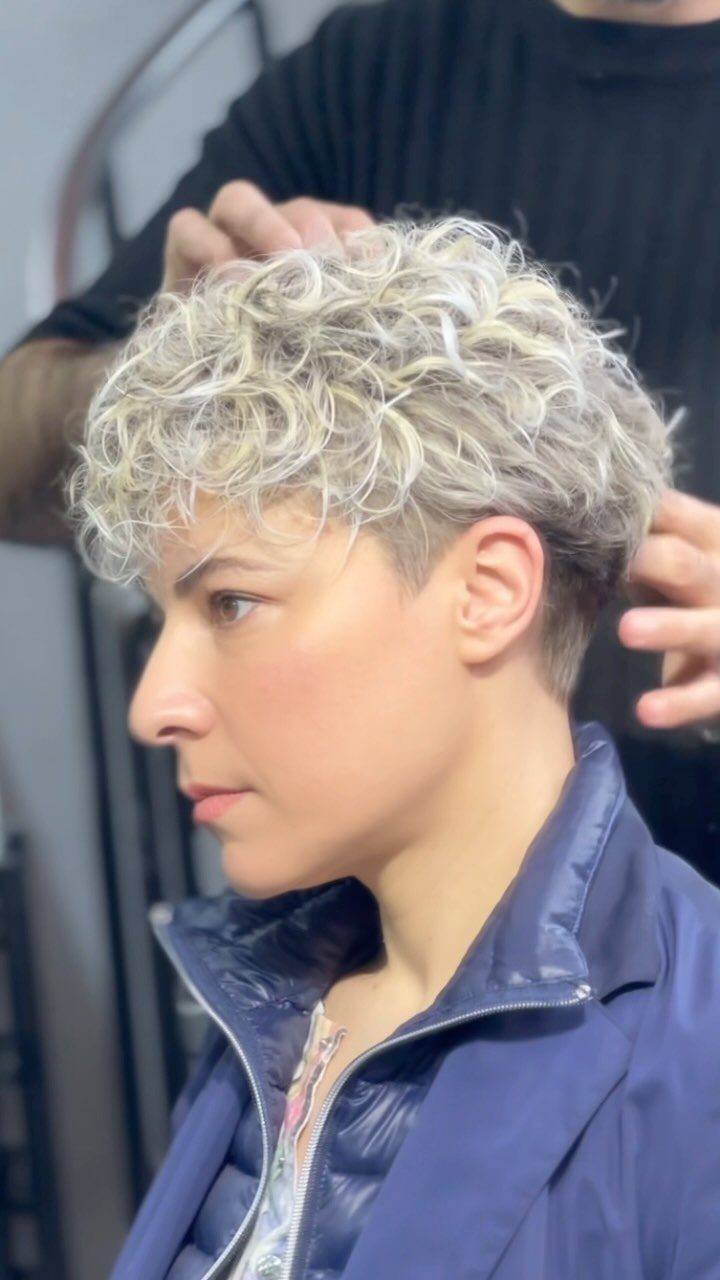 Short silver-blond curly pixie cut styled by hands in a salon