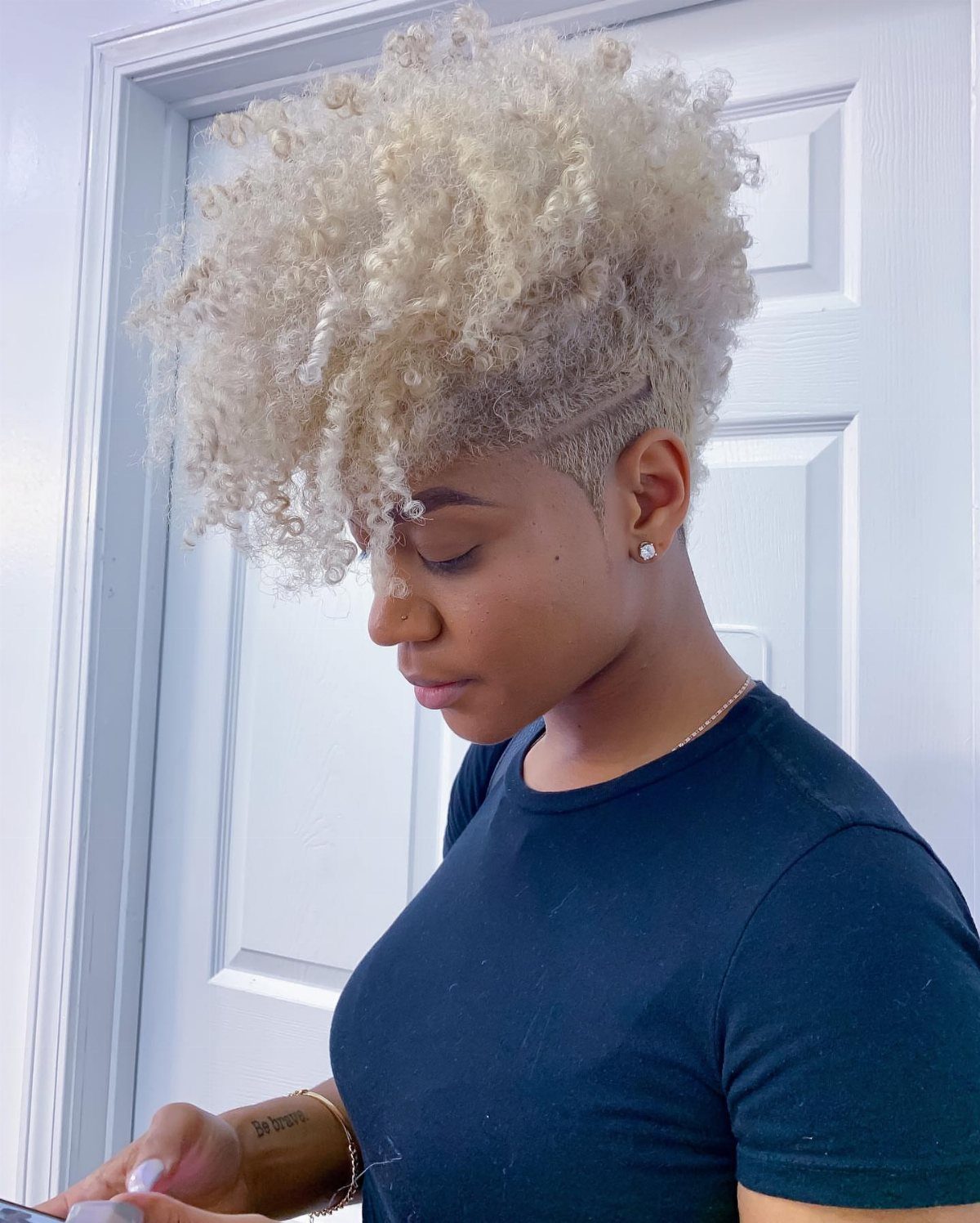 Person with pale blond curls and shaved sides looking down at a phone