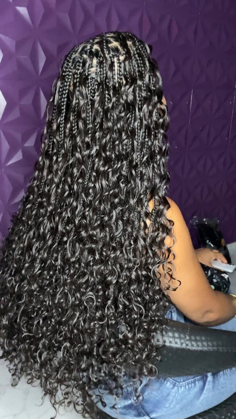 Long black crochet goddess braids cascade in curls down a seated person's back.