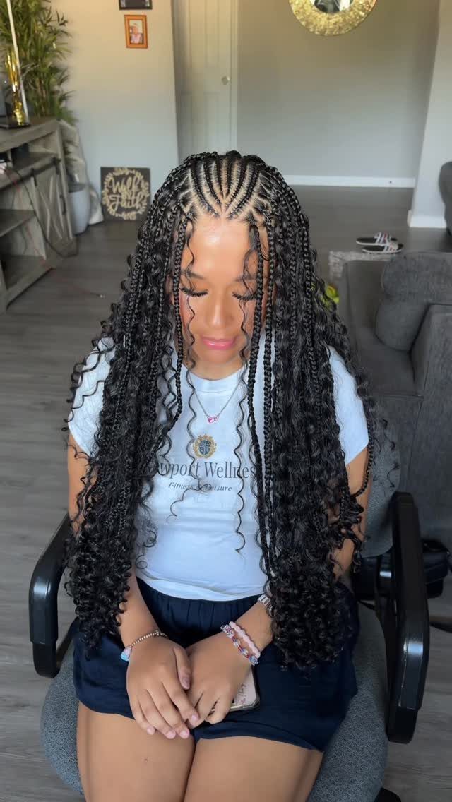 Long knotless braids with loose curly ends frame a seated woman's face