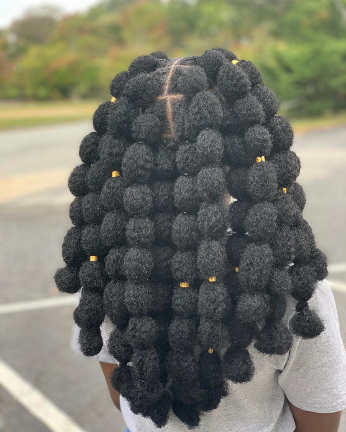 Long black cornrow bubble braids with gold beads viewed from behind