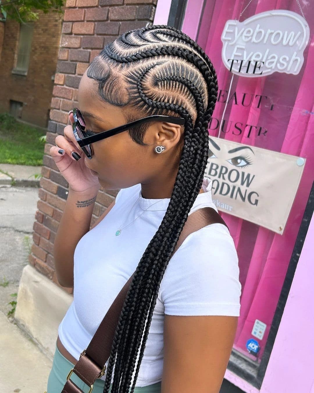 Curved black stitch braids sweep across the scalp into long plaits