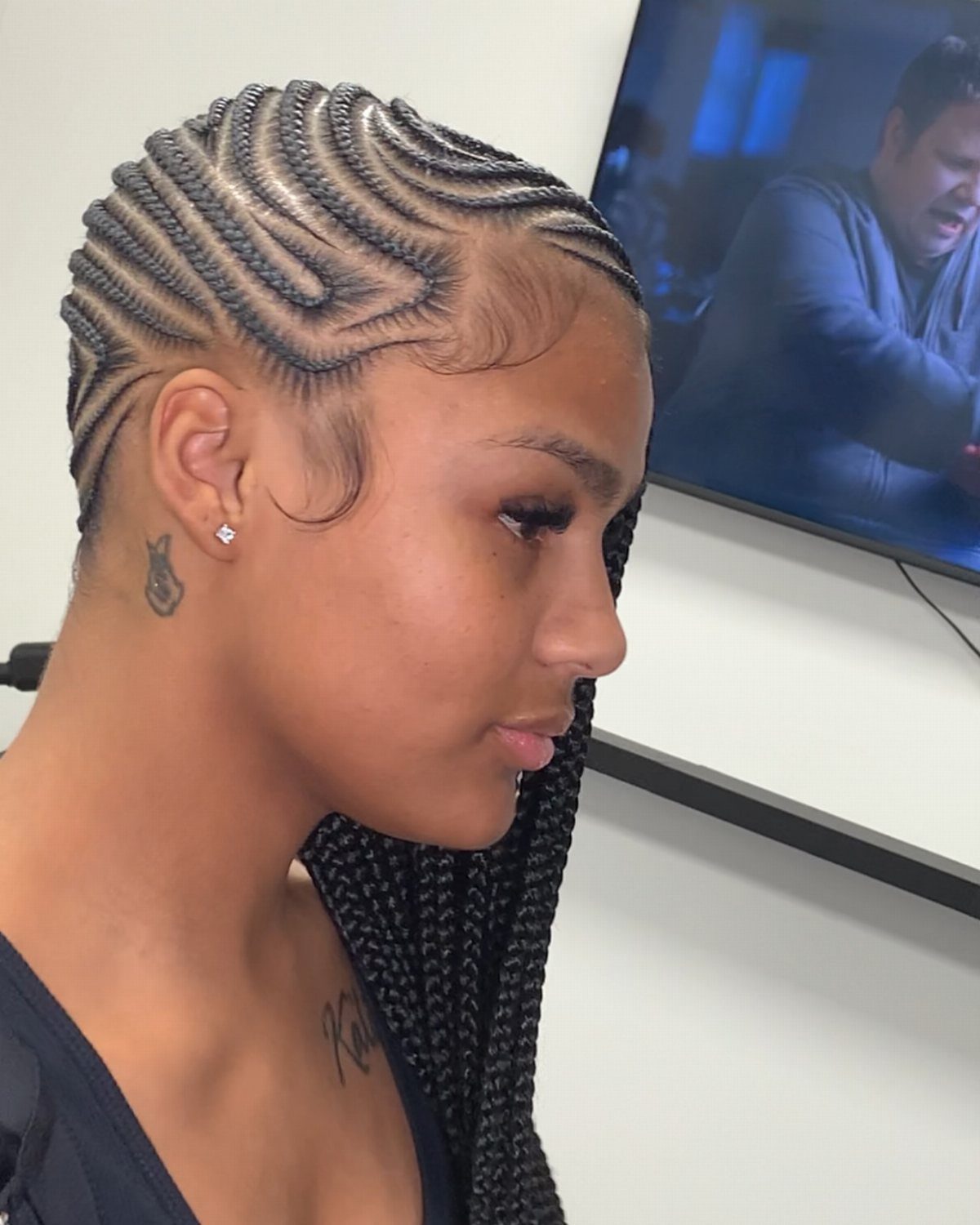Side-swept cornrows curve across the scalp into long braids over one shoulder