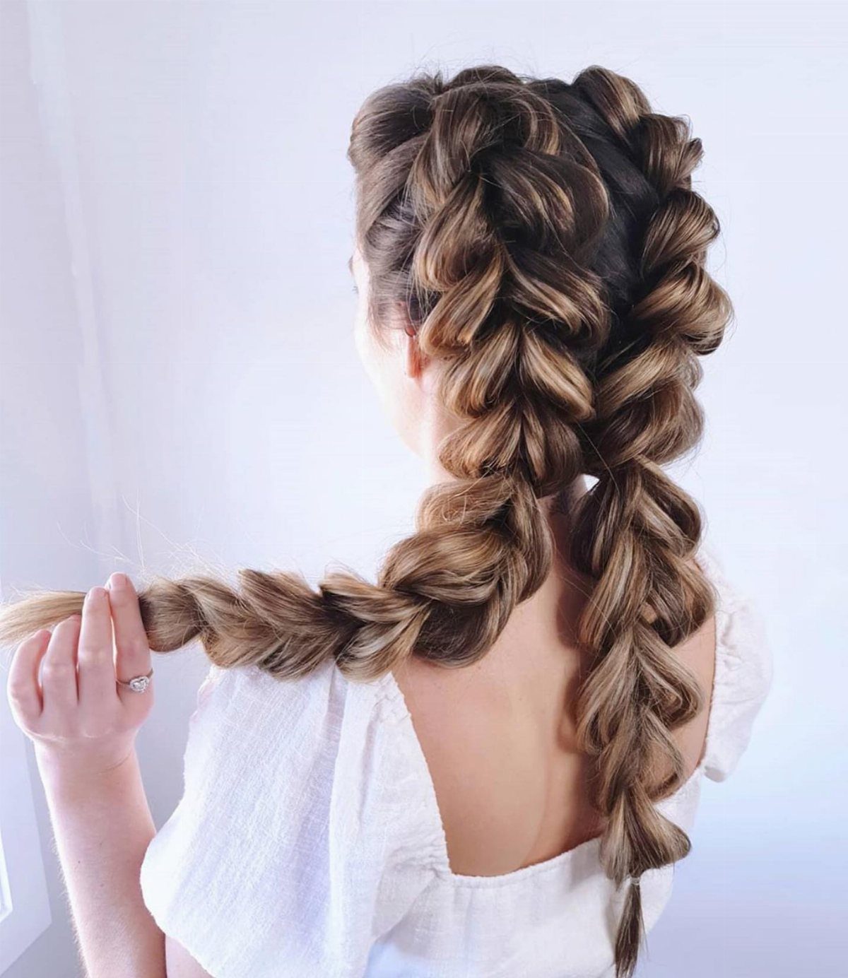 Thick brown braided pigtails hang down the back of a person wearing white.
