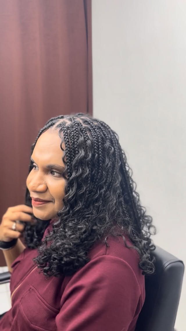 Scalp braids blend into long, loose curls on a seated woman