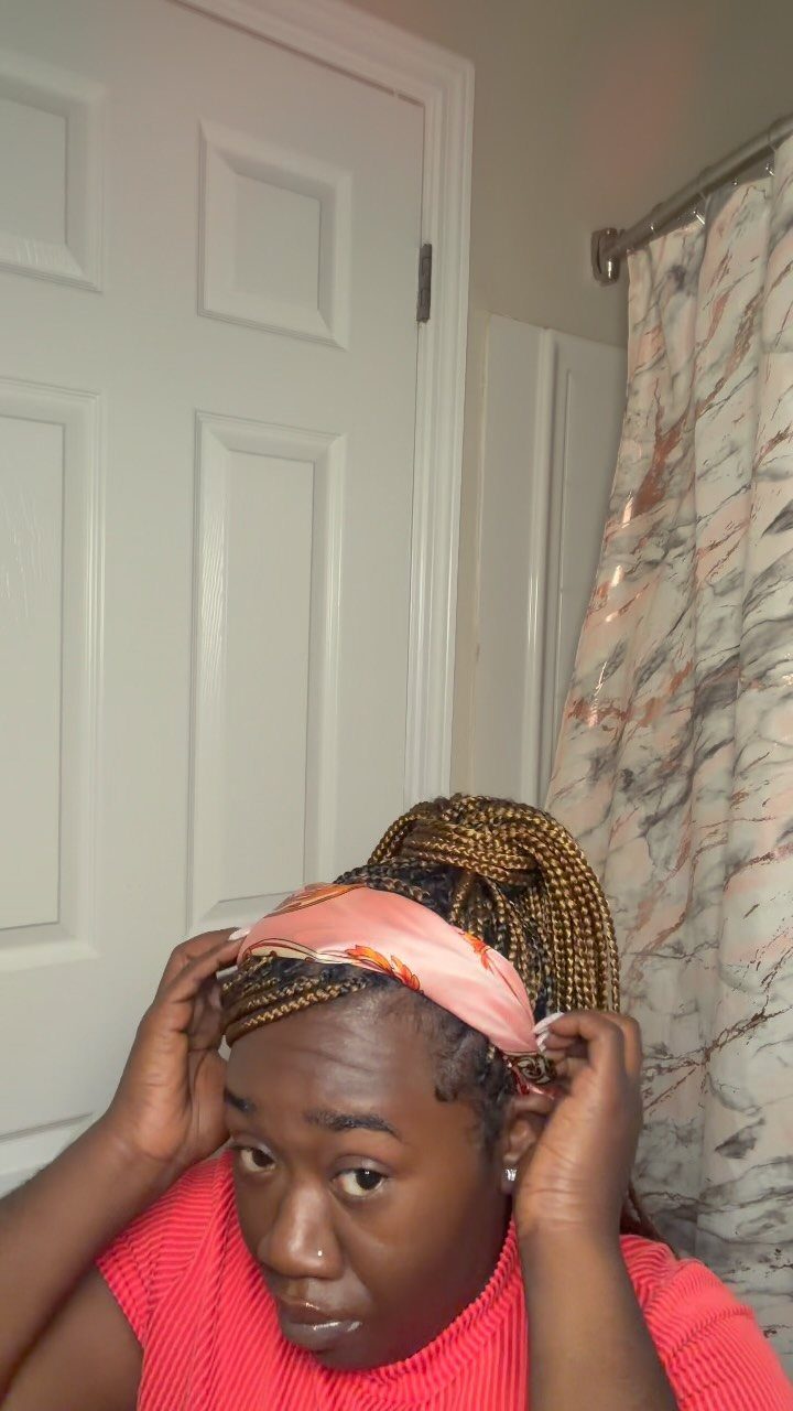 Person tying a pink scarf over long dark and blonde box braids