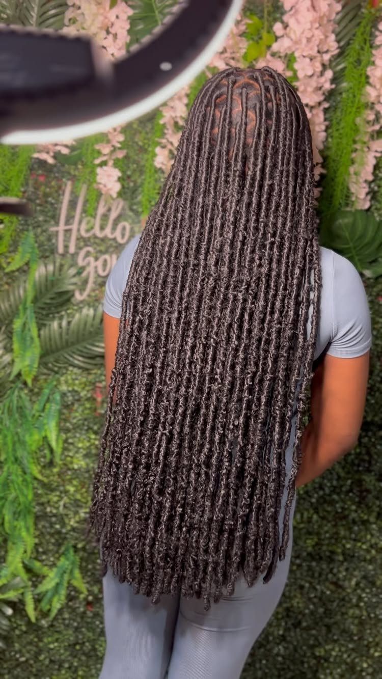 Long dark locs cover the back of a person wearing pale blue-gray clothes