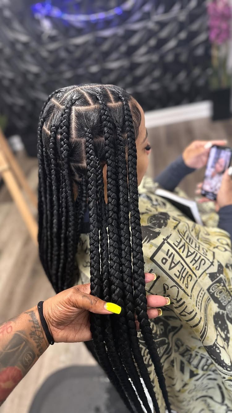 Long black individual braids hang from neatly sectioned roots as a hand holds them
