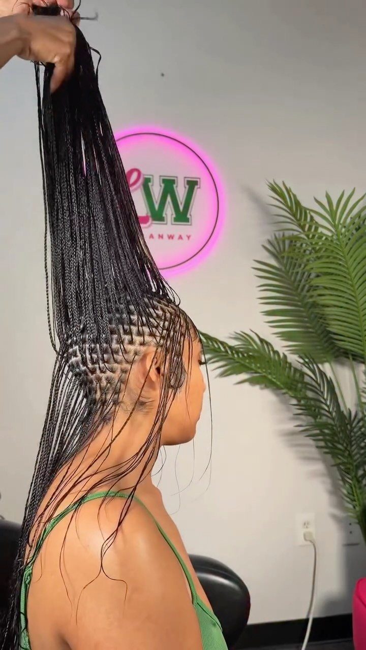 Fine micro braids being gathered on a seated person beside a plant