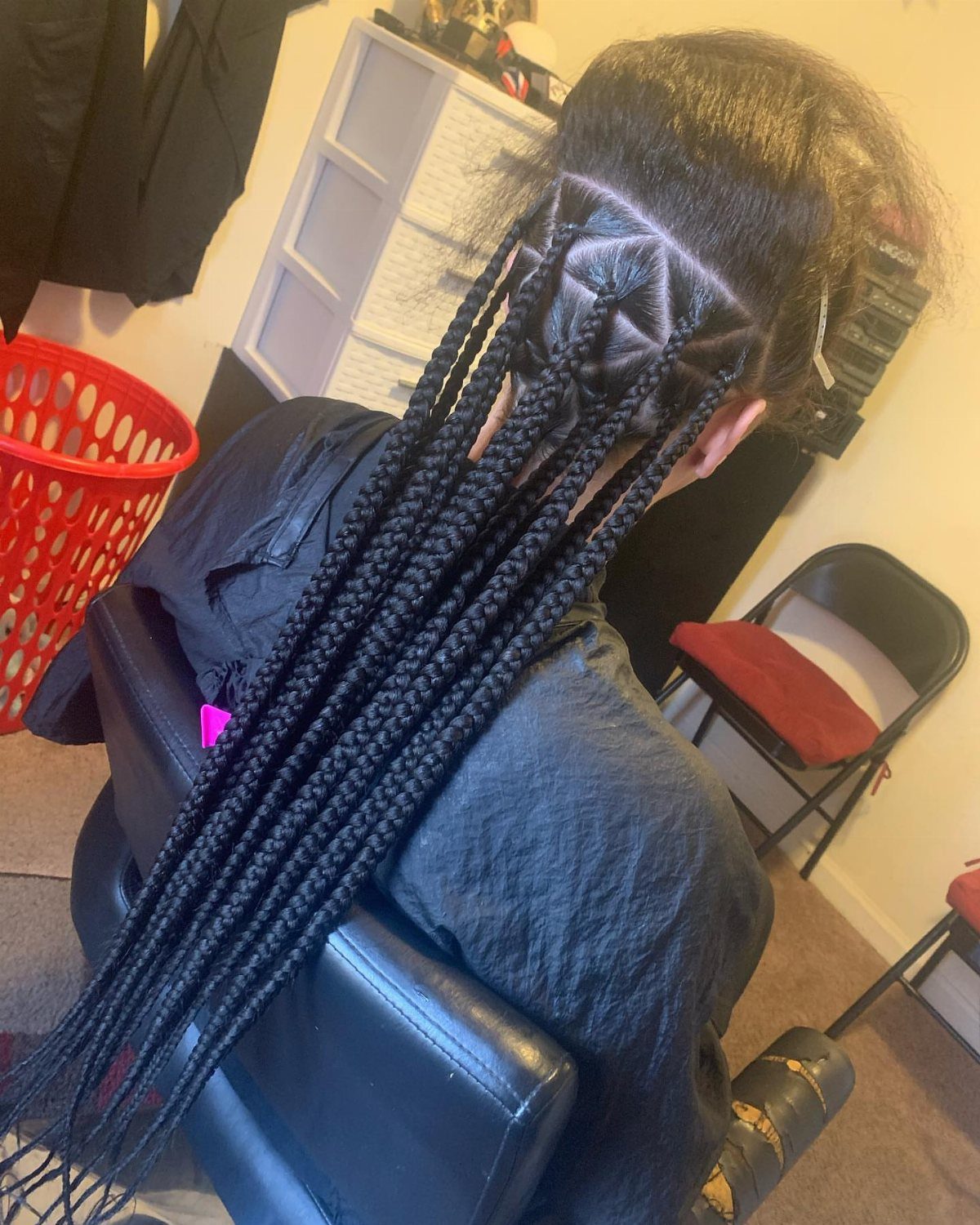 Long black braids emerge from triangular scalp sections on a seated person
