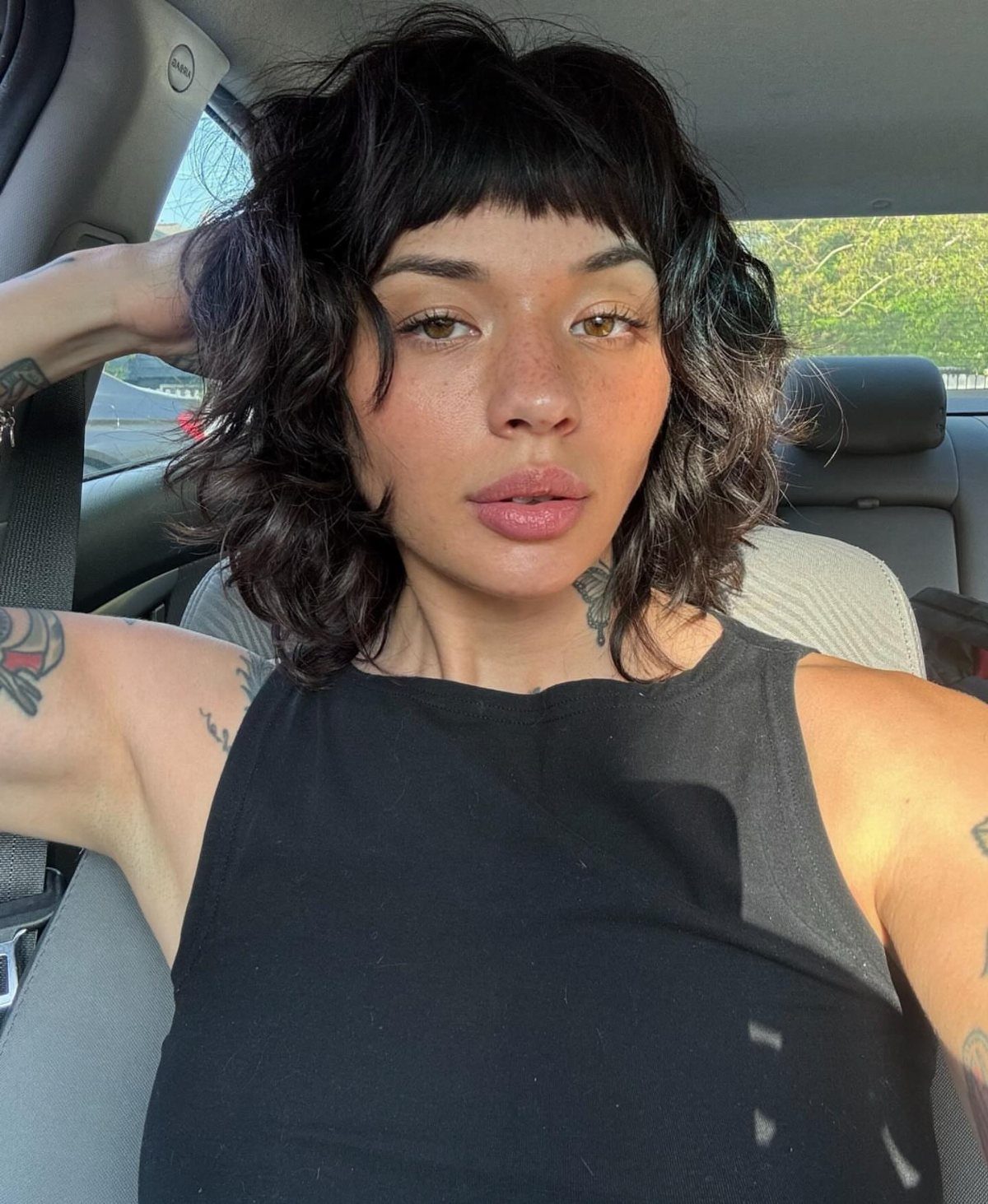 Person showing a chin-length curly bob with short bangs in a car