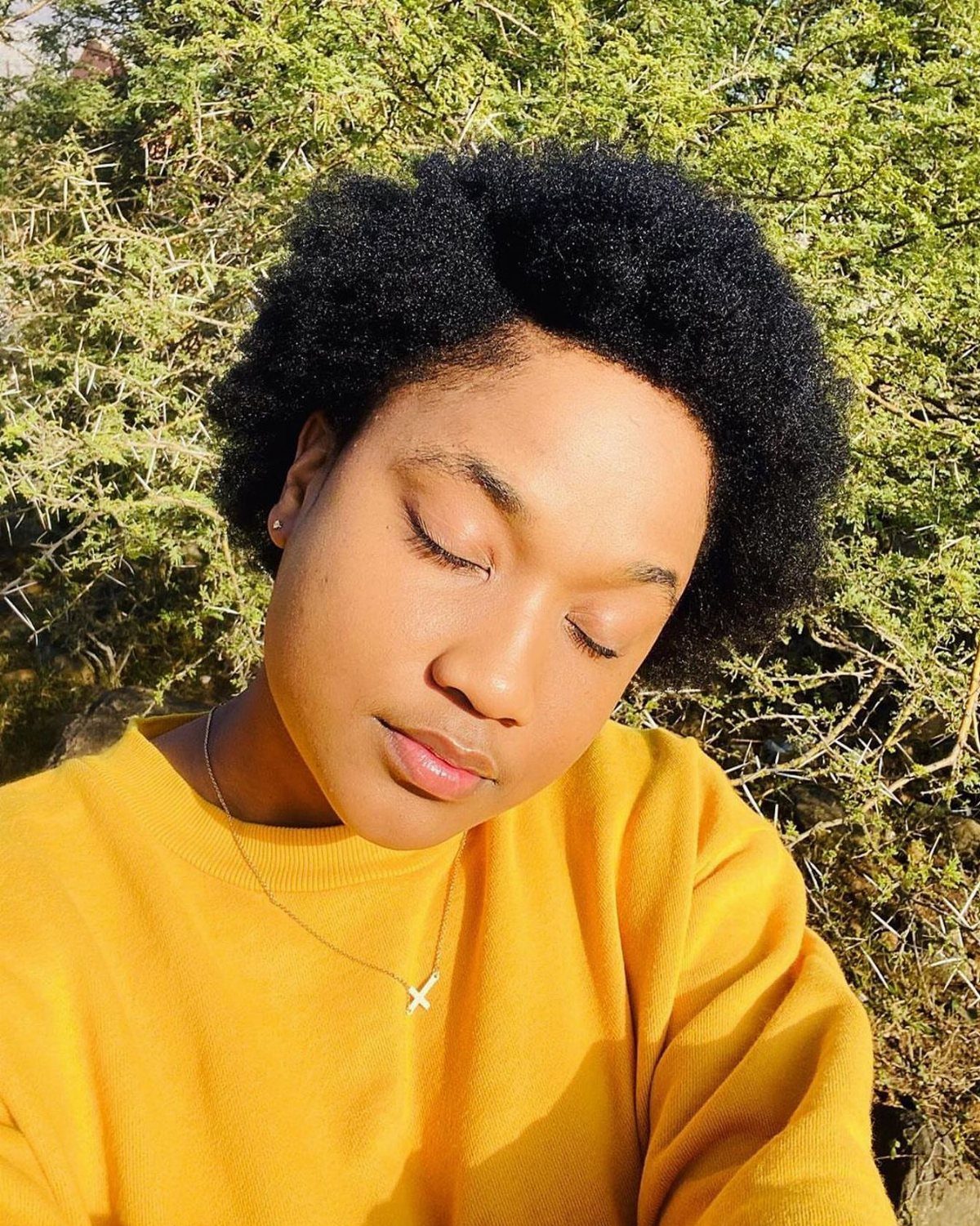Person with a rounded, short natural afro wearing a mustard-yellow top outdoors