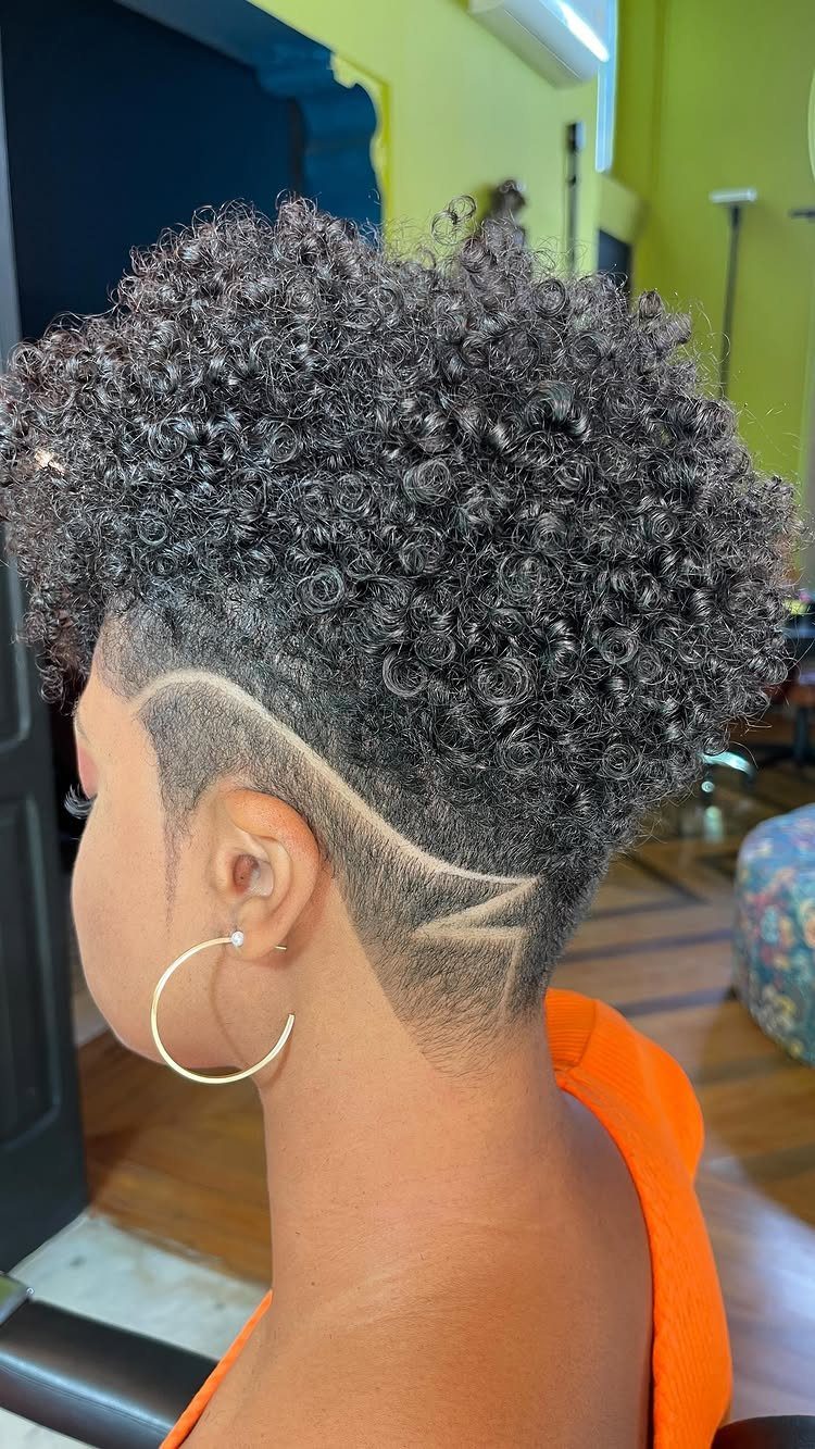 Rounded tightly curled top with shaved sides and a curved hair design