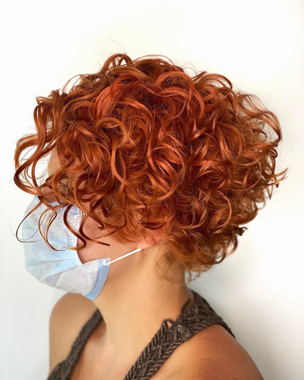 Voluminous copper curls sweep forward over shorter hair at the back