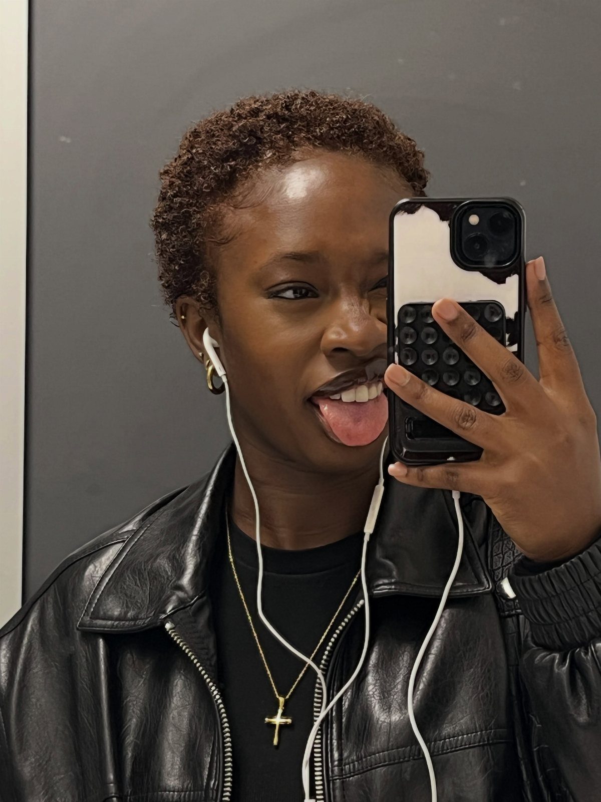 Person with a short natural Afro taking a mirror selfie in a leather jacket