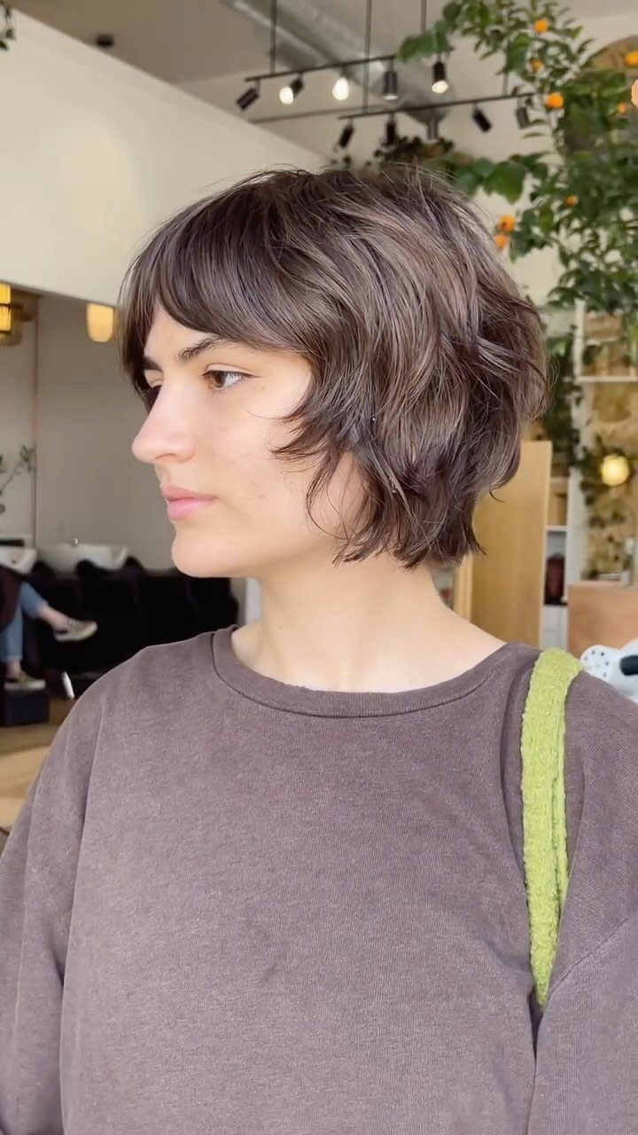 Short, textured brown bixie haircut shown in profile in a salon