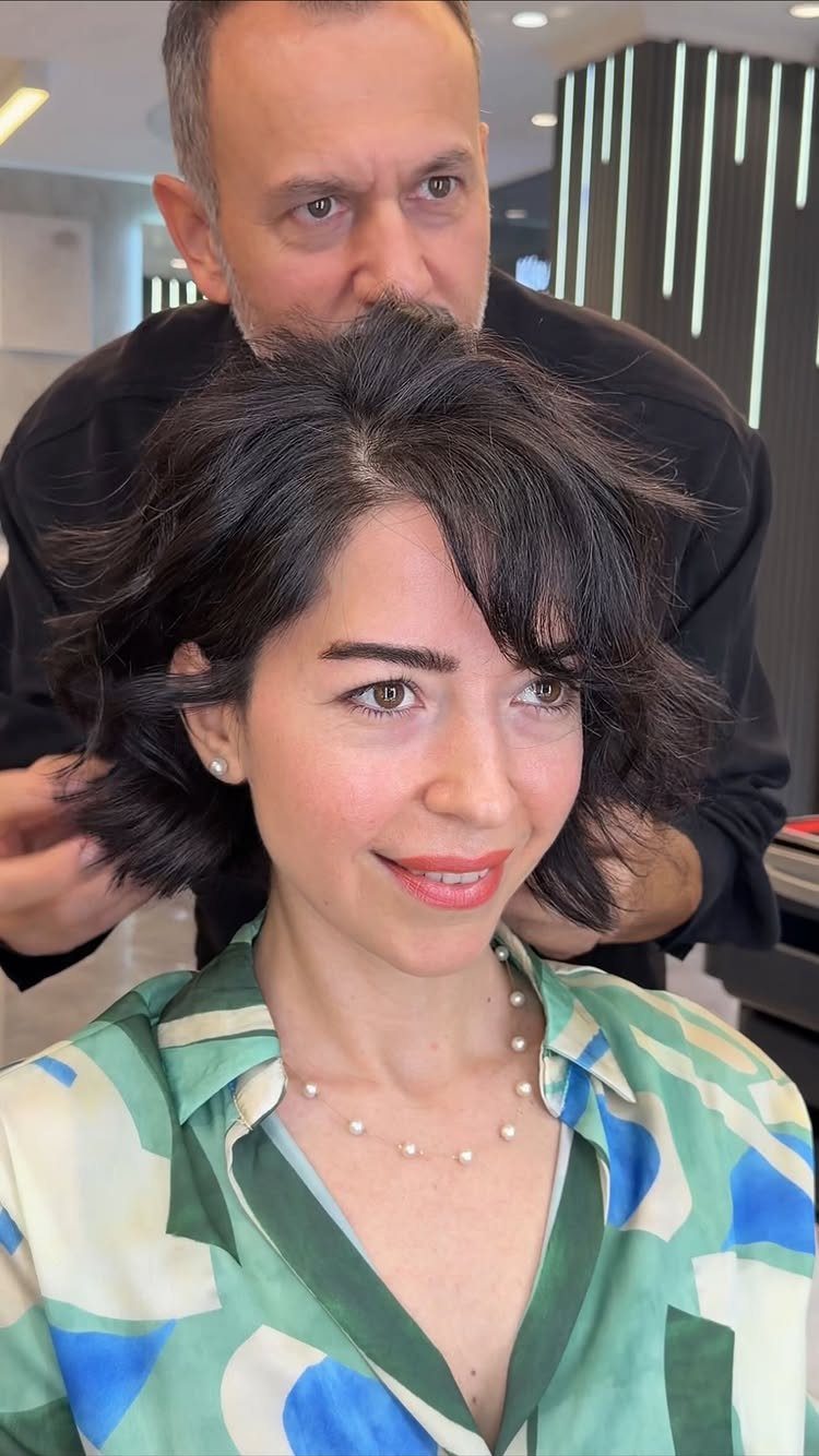 Woman showing a dark shaggy bob with side-swept bangs in a salon