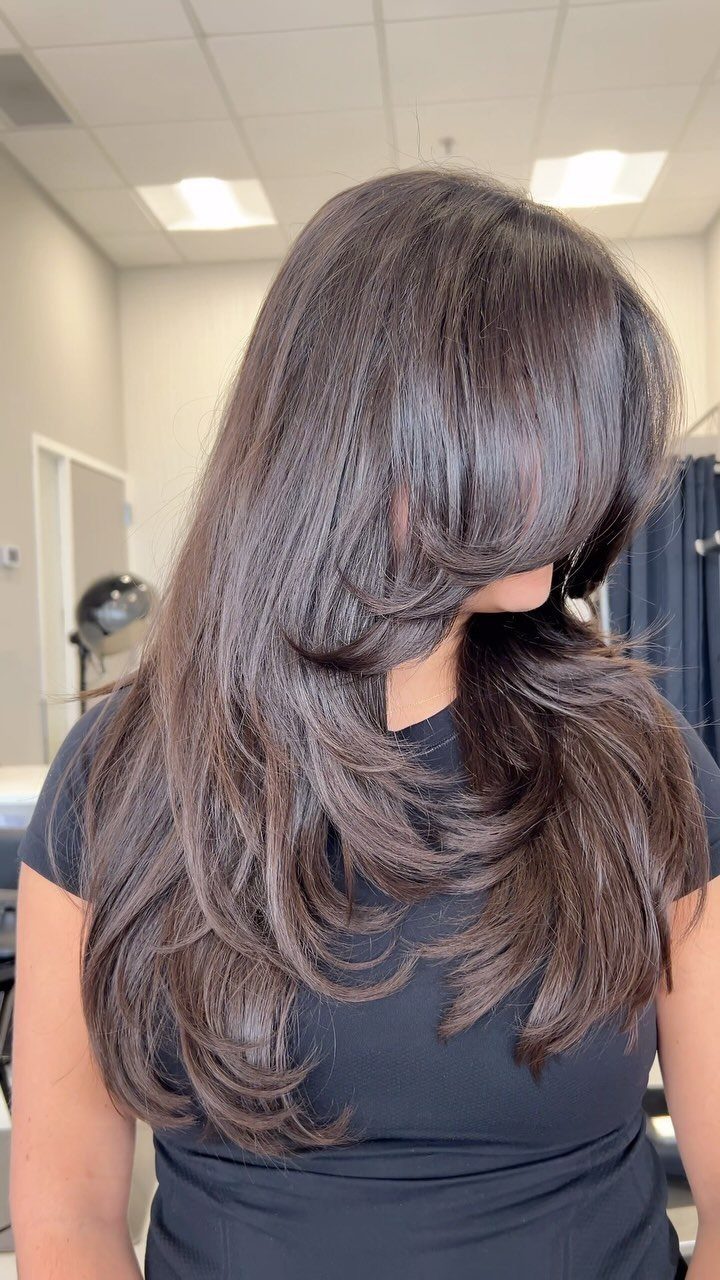 Long dark hair with cascading face-framing layers shown from the side in a salon