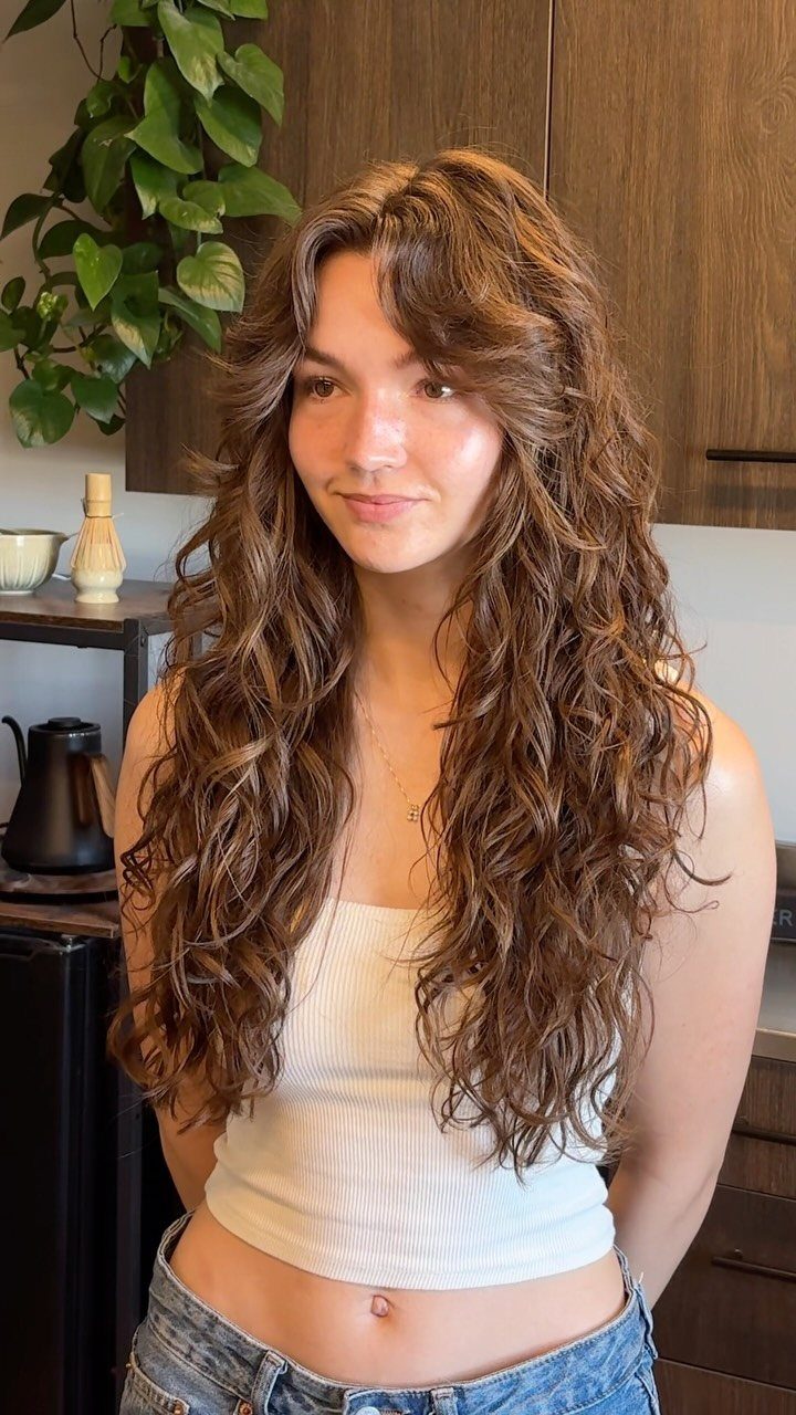 Woman showcasing long loose layered brown waves with wispy bangs indoors