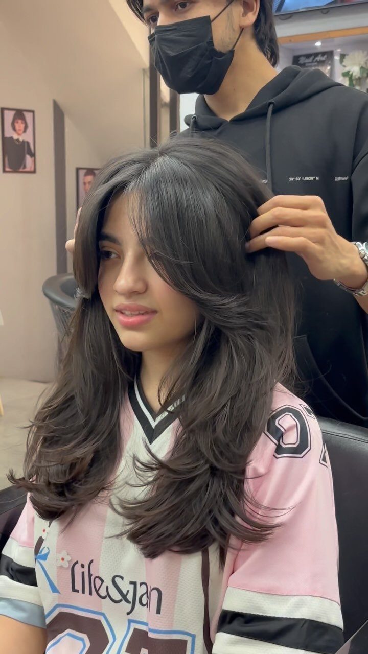 Woman showing medium-length face-framing layers with dark wavy hair in a salon