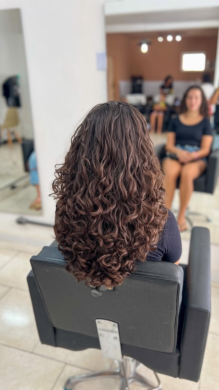 Shoulder-length dark spiral curls shown from behind in a salon chair
