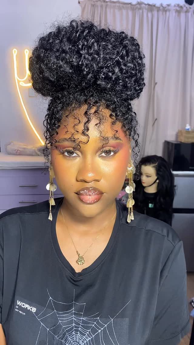 Woman wearing a high curly bun with loose forehead curls and dangling earrings