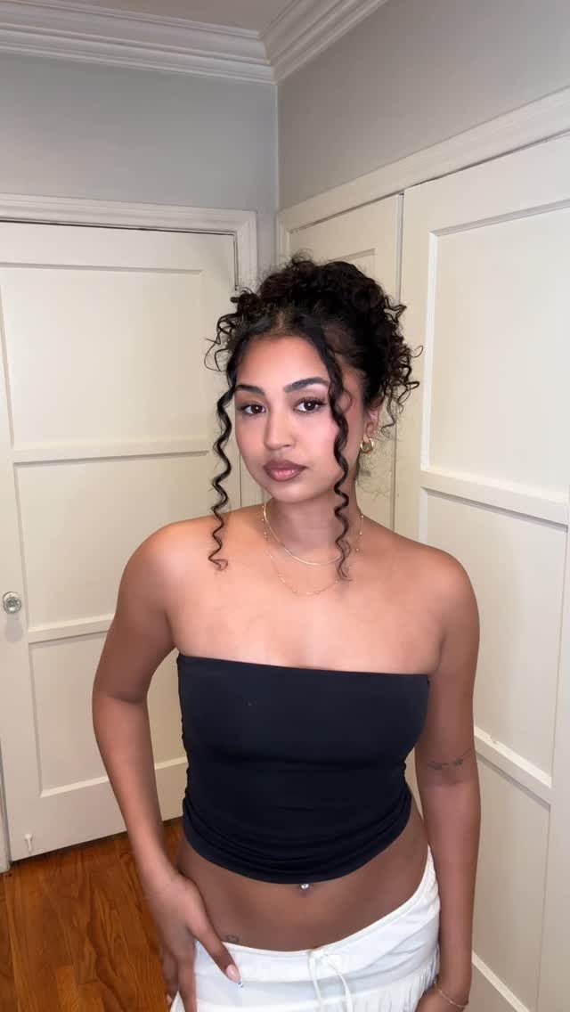Woman with curly hair in a high bun and loose face-framing tendrils