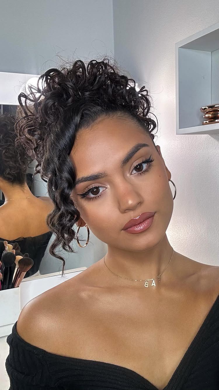 Woman wears a high curly puff with loose curls framing her face