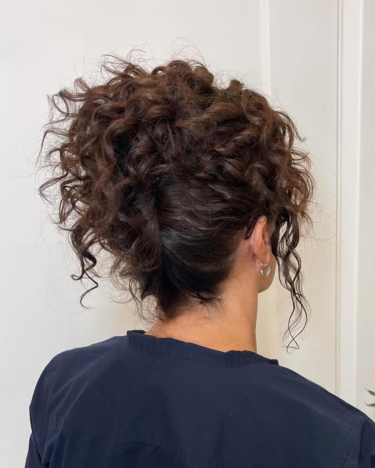 Curly hair pinned upward into a voluminous loose updo with tendrils