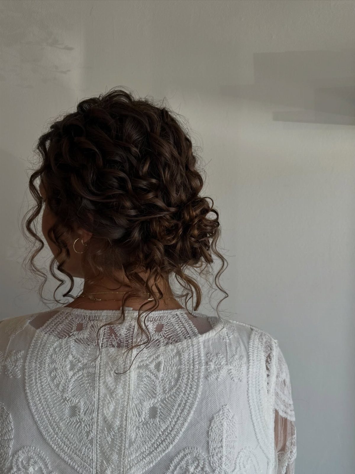 Curly hair gathered into a loose low bun with tendrils at the nape