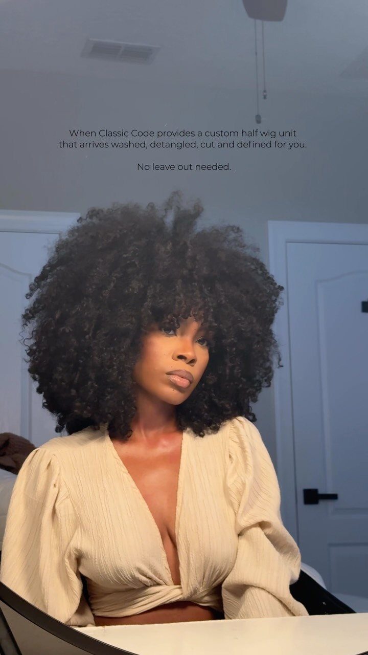 Woman with a rounded afro poses in a cream blouse indoors